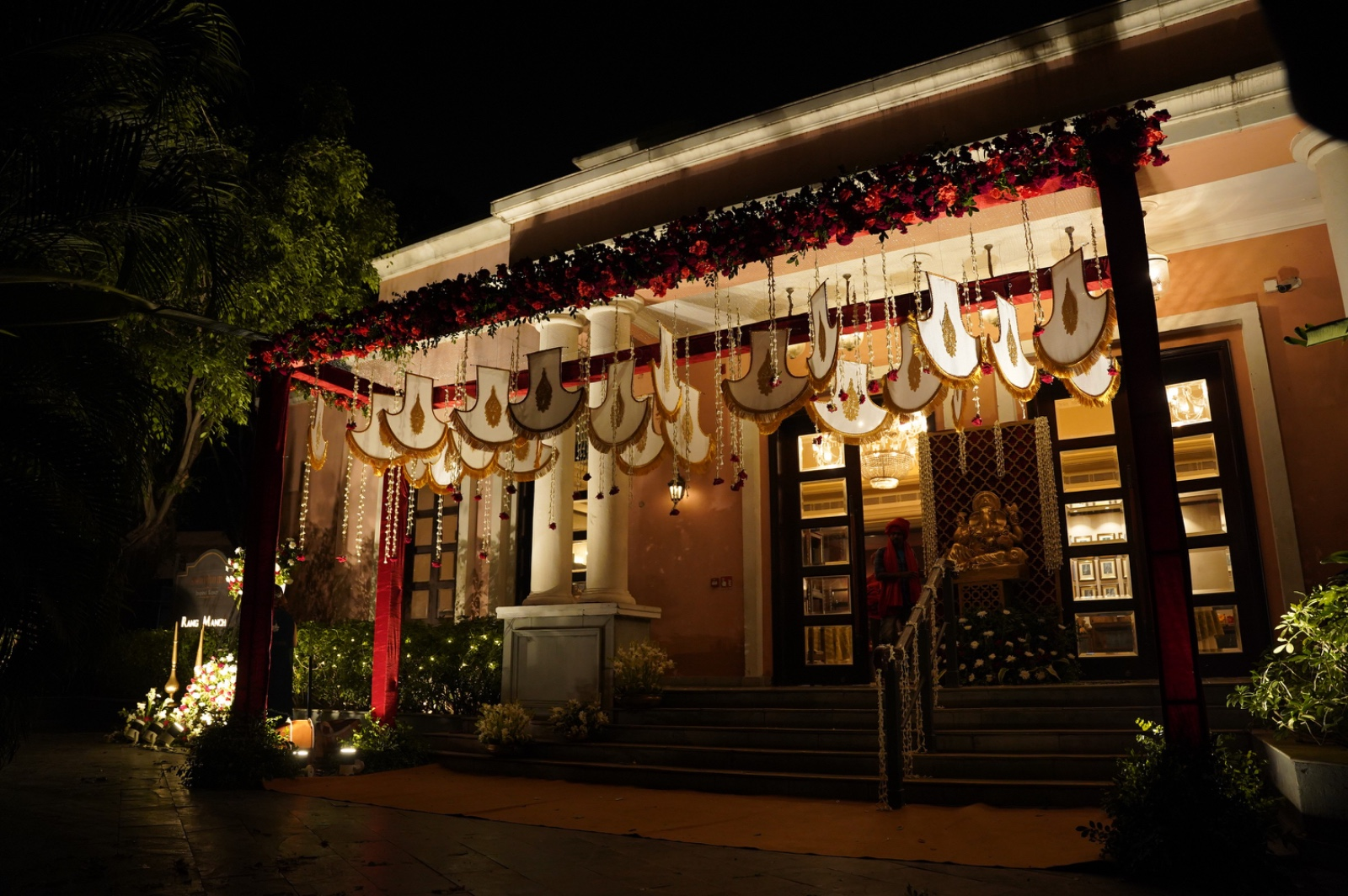 Ceremonial entrance canopy with red florals, ornate draping, and a lit Ganesha focal point