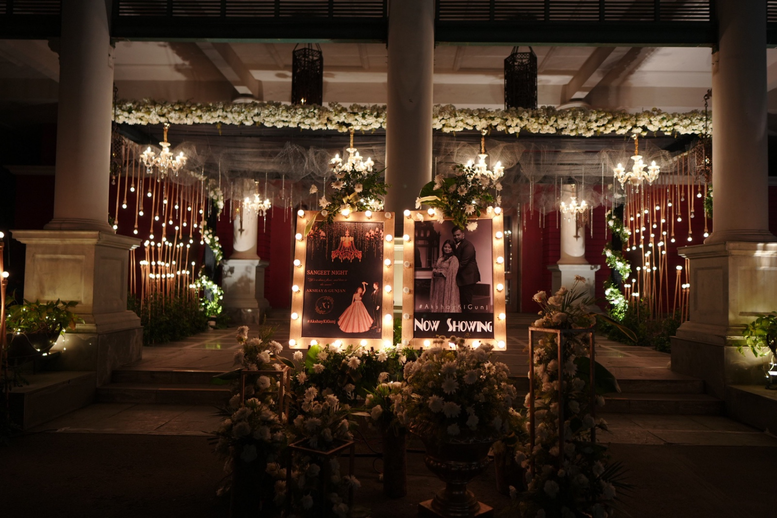 Nighttime celebration entrance with illuminated couple portraits and hanging lights